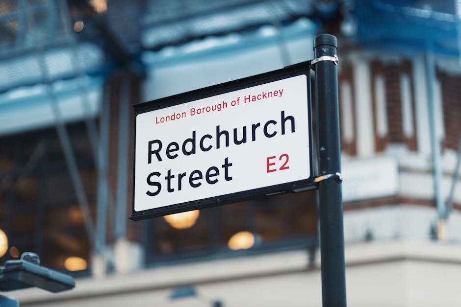 Close-up of a rectangular street sign for Redchurch Street in the London Borough of Hackney, with a white background and black text. The sign features the name 'Redchurch Street' prominently, with 'Lo